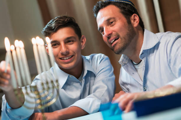 About a father and his teenage son celebrating hanukkah, lighting the menorah.